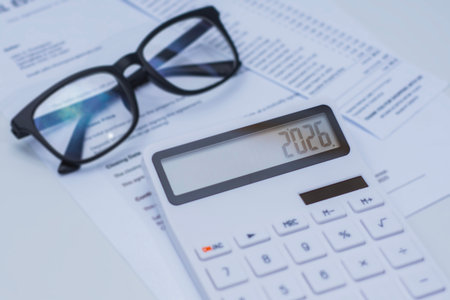 White calculator displaying the number 2026, placed on financial documents with black eyeglasses nearby. Concept business planning and tax calculationの写真素材