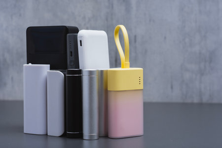 A group of power banks in various shapes, sizes, and colors on a table. Concept portable charging solutions, mobile technology, and on-the-go energy backup for smartphones and devicesの写真素材