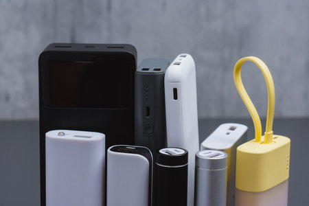 A group of power banks in various shapes, sizes, and colors on a table. Concept portable charging solutions, mobile technology, and on-the-go energy backup for smartphones and devicesの写真素材