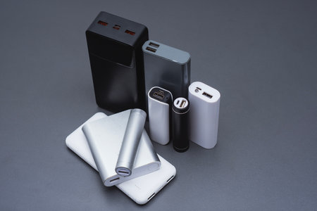 A group of power banks in various shapes, sizes, and colors on a table. Concept portable charging solutions, mobile technology, and on-the-go energy backup for smartphones and devicesの写真素材
