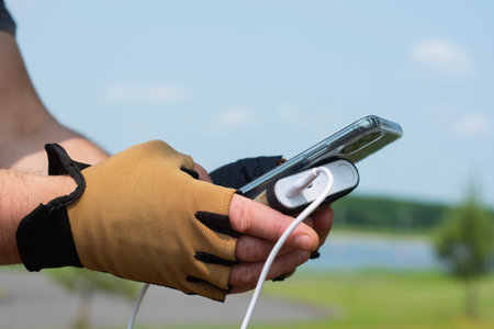 Close-up of a person wearing half-finger cycling gloves, charging a smartphone with a power bank in nature. Concept mobility, active lifestyle, and technology on the goの写真素材