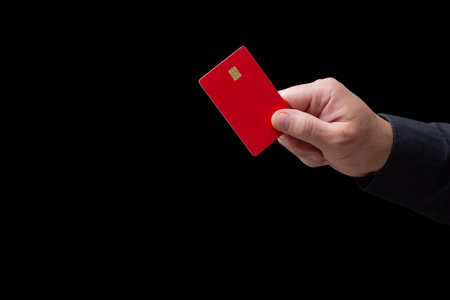 Close-up of a hand holding a red credit or debit card with chip on a black background. Concept of banking, finance, contactless payment and online shoppingの写真素材