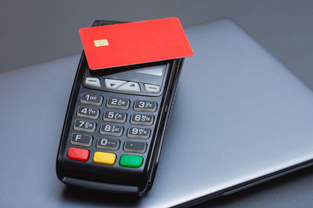 A red credit card on a payment terminal next to a laptop. Secure online transactions in e-commerce,...