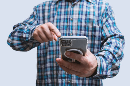Man in a plaid shirt holding smartphone with blank screen on light background. Portable mobile technology conceptの写真素材