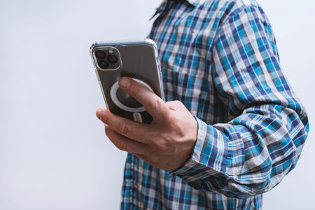 Man in a plaid shirt holding smartphone with blank screen on light background. Portable mobile...