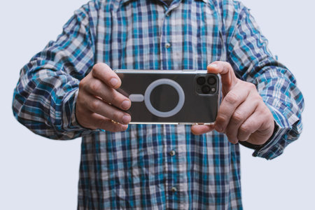 Close-up of a man in a plaid shirt taking a photo with a modern smartphone in landscape mode. Mobile photography, tech usage and content creationの写真素材
