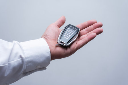 Close -up man holds a man with a white shirt in his hand, a luxurious car key on a light background....