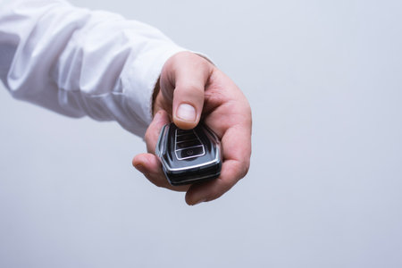 Close -up man holds a man with a white shirt in his hand, a luxurious car key on a light background. The concept of a new premium carの写真素材