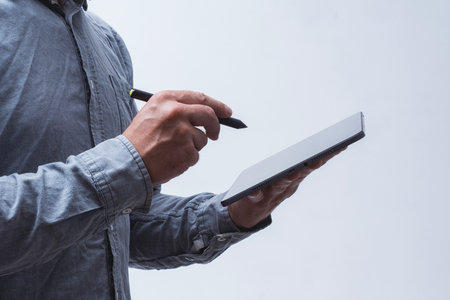 Close-up of male hands holding a modern tablet with digital stylus on a light background. Concept of digital document signing, online services, business communication and electronic paperworkの写真素材