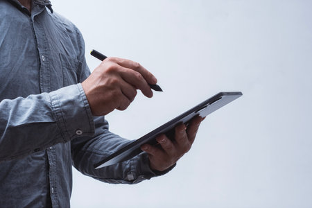 Close-up of male hands holding a modern tablet with digital stylus on a light background. Concept of...