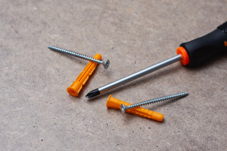 Close up of a manual screwdriver with metal screws and orange wall plugs on a wooden surface. Concept of DIY tools, construction equipment for home repair and installationの写真素材