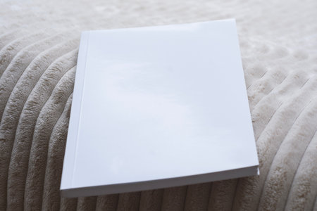 Minimalistic mockup of a blank magazine or catalog with white cover on a cozy beige blanket. Template for showcasing book cover design, brochure layout, catalog presentation, or branding projectsの写真素材