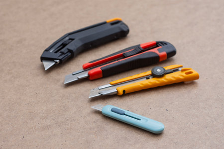 Set of utility knives and box cutters of different colors lying on a wooden surface. Concept of construction tools, office equipment, and DIY craftsの写真素材