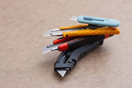 Set of utility knives and box cutters of different colors lying on a wooden surface. Concept of construction tools, office equipment, and DIY craftsの写真素材