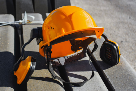 Yellow safety helmet with attached ear defenders lying on concrete blocks at a construction site. Concept workplace safety, industrial protection gear and professional equipment used by buildersの写真素材