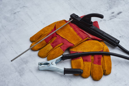 Welding electrode holder and protective gloves lie on a gray industrial surface. Concept welding...