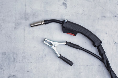 Close-up of a welding torch and ground clamp on a gray concrete surface. Industrial concept metalworking, repair work, and professional engineering toolsの写真素材