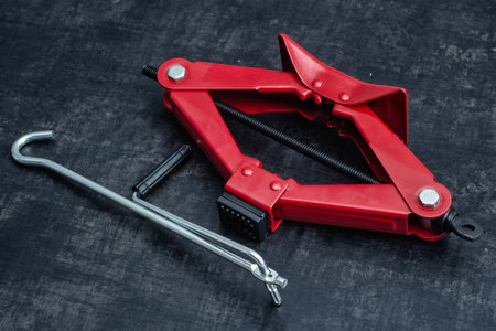 Close-up of a red car jack with a metal handle tool on a dark textured background. Concept of automotive repair, maintenance, garage tools and mechanical equipmentの写真素材