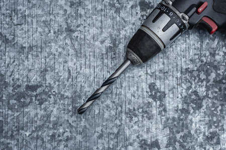 Close-up of a cordless electric drill with a metal drill bit on a textured steel background. Concept of construction, DIY, home improvement, and professional toolsの写真素材