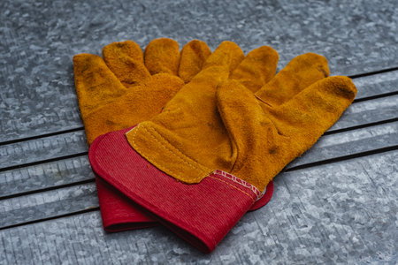Pair of protective leather and fabric work gloves on a galvanized metal background. Industrial safety equipment concept for construction, workshop, handyman and DIY projectsの写真素材