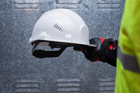White protective safety helmet held by a worker wearing a reflective vest. Concept of industrial...
