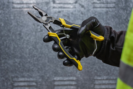 Construction worker wearing protective gloves and safety vest holding metal pliers. Concept of...