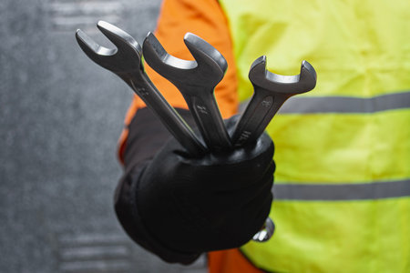 Close-up of a construction worker wearing safety gloves and reflective vest holding several metal...