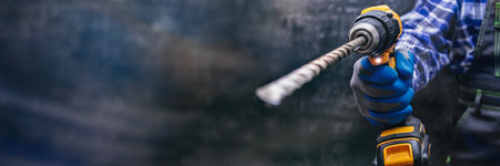 Close-up of a construction worker holding a power drill with a metal bit, pointed toward the camera. Concept for professional craftsmanship, renovation and industrial safetyの写真素材
