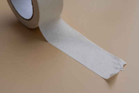 White adhesive tape roll on neutral beige background. Concept repair and DIY, first aid supply, packaging material and clean copy space