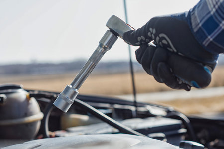 Mechanic gloved hand in blue protective work glove holds a metallic ratchet wrench with socket...