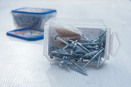 Close up of metal screws with plastic storage box on wooden surface. Construction and repair...