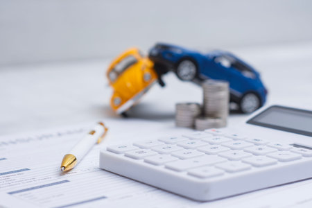 Concept auto insurance claim and financial compensation. Document for vehicle insurance application with crashed toy cars and calculator on office table representing risk management