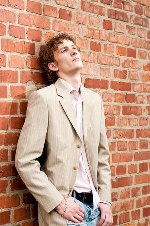 A handsome young man in a light-coloured suit posed against a brick wall, relaxed and dreamy, reflecting on his lifeの写真素材