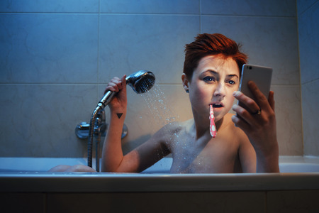 Young woman totally mesmerized by her phone in the middle of taking a bath.