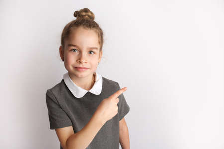 Attractive little girl in a strict school dress, stands on a white background with empty copy space, gestures with her hands, admires a happy expression on her faceの写真素材
