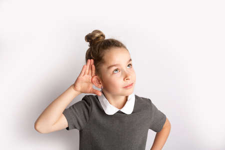 Attractive little girl in a strict school dress, stands on a white background with empty copy space, gestures with her hands, admires a happy expression on her faceの写真素材