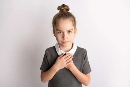 Attractive little girl in a strict school dress, stands on a white background with empty copy space, gestures with her hands, admires a happy expression on her faceの素材 [FY310165835191]