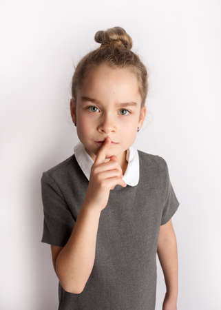 Attractive little girl in a strict school dress, stands on a white background with empty copy space, gestures with her hands, admires a happy expression on her faceの写真素材