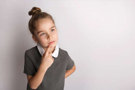 Attractive little girl in a strict school dress, stands on a white background , gestures with her hands, admires a happy expression on her faceの写真素材