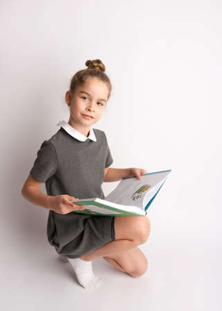 Attractive little girl in a strict school dress, stands on a white background with empty copy space, gestures with her hands, admires a happy expression on her faceの写真素材