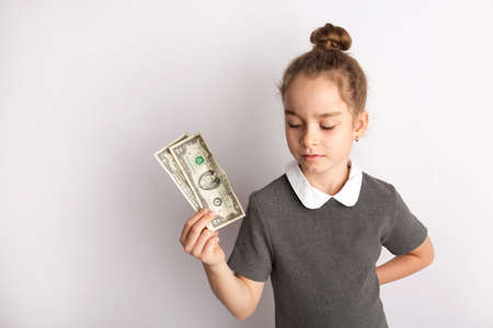 Attractive little girl in a strict school dress, stands on a white background , gestures with her hands, admires a happy expression on her faceの写真素材