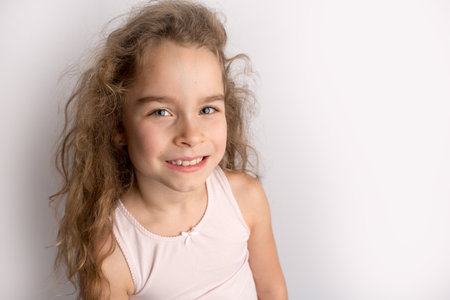 Attractive little girl stands on a white background with empty copy space, happy expression on her face with a beautiful smile, children crooked teeth, pediatric dentistryの写真素材