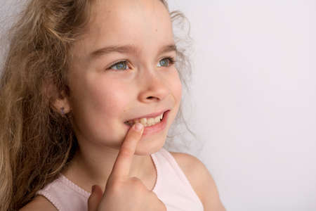 Attractive little girl stands on a white background with empty copy space, happy expression on her face with a beautiful smile, children crooked teeth, pediatric dentistryの写真素材