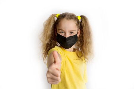Child in a yellow shirt in a black mask from covid on a white backgroundの写真素材