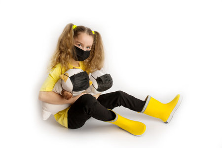 Girl in a yellow t-shirt and black mask covid19 on a white background with toys in a black covid maskの写真素材
