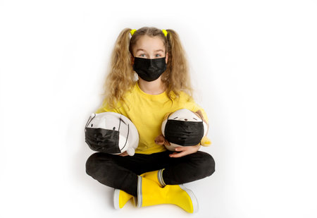 Girl in a yellow t-shirt and black mask covid19 on a white background with toys in a black covid maskの写真素材