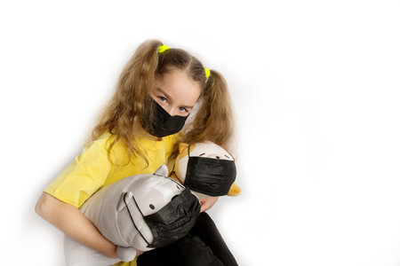 Girl in a yellow t-shirt and black mask covid19 on a white background with toys in a black covid maskの写真素材