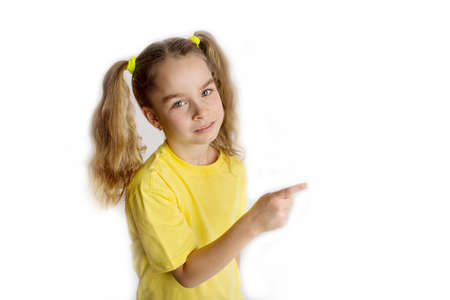 Little blonde girl in a yellow t-shirt makes gestures, isolated on a white background childrens studio portrait. Childhood lifestyle conceptの写真素材