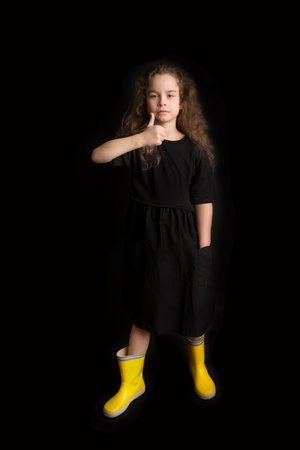Portrait of pretty cheerful girl, in black and yellow clothes, isolated on black background. Childrens emotionsの写真素材