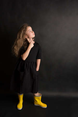 Portrait of pretty cheerful girl, in black and yellow clothes, isolated on black background. Childrens emotionsの写真素材